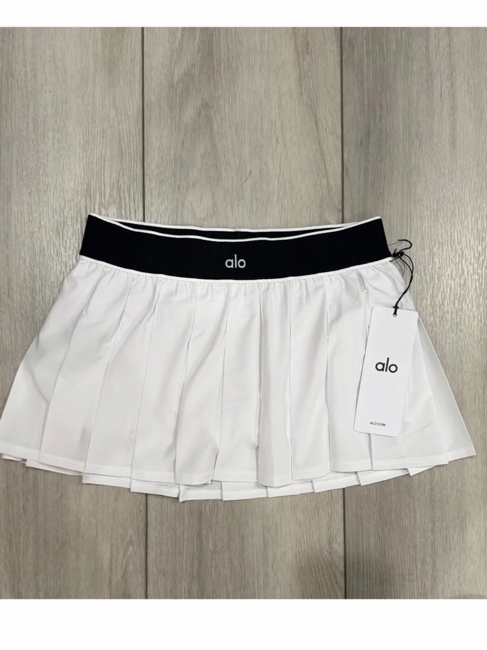 alo Yoga Low Rise AMP It Up Tennis Skirt in White with Black Waistband. SIZE: S